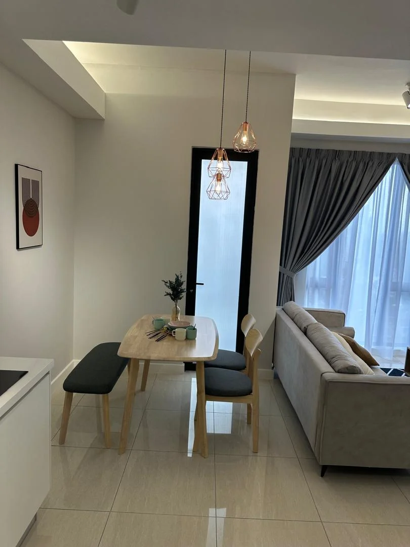 Dining features: light wood dining table, 2 wooden chairs with grey cushions, pendant lighting fixtures, white walls, glossy tile flooring, floor-to-ceiling windows with sheer curtains, grey drapes, sofa in living area visible, decorative wall art; style: modern.